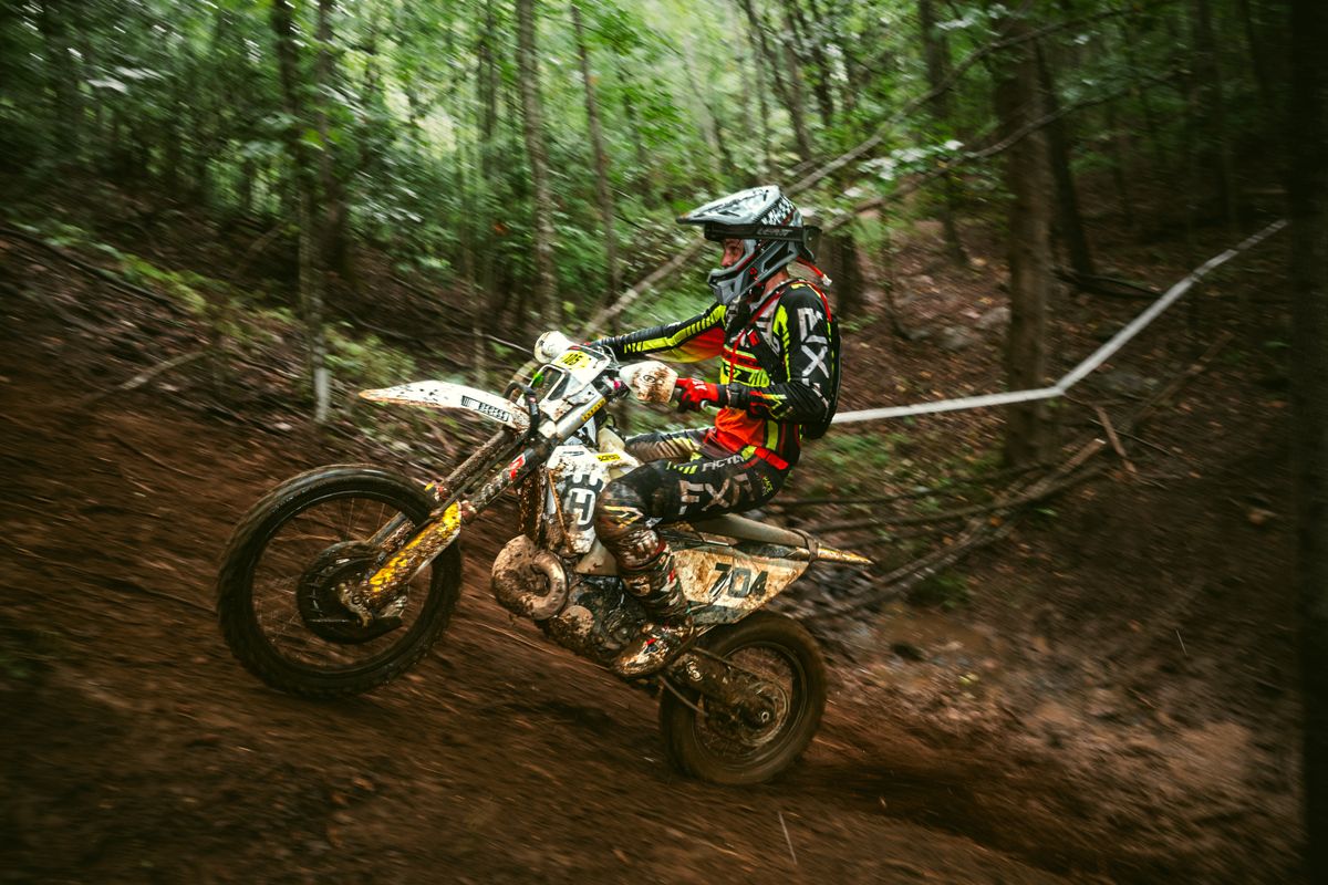 Devon racing a dirt bike up a muddy, wooded hill during an enduro event